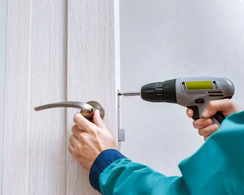 A Technician Is Using A Power Drill To Install A Lever Lock On The Door Of An Office.